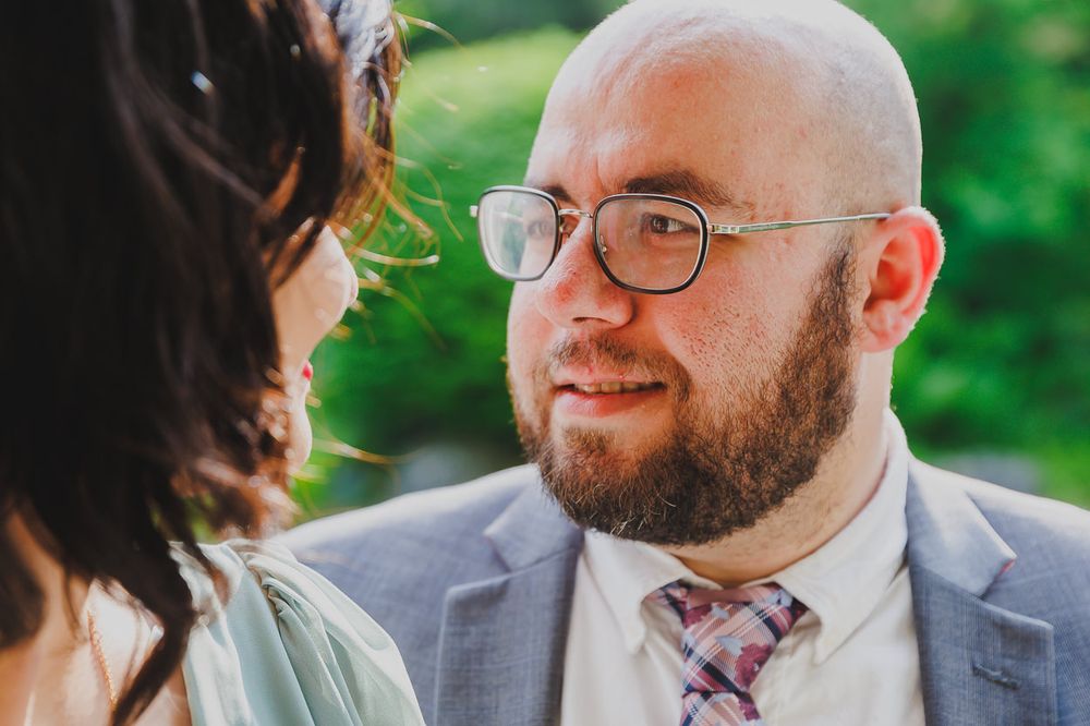 A sweet moment captured between a couple in formal attire against a green garden background.