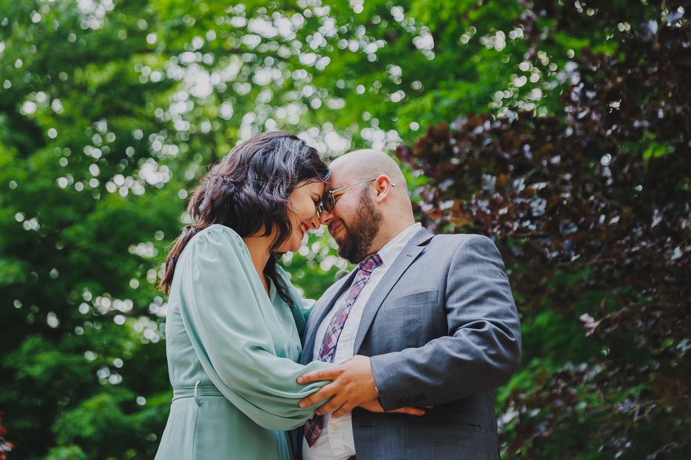 A tender moment between a couple in formal attire surrounded by lush greenery.