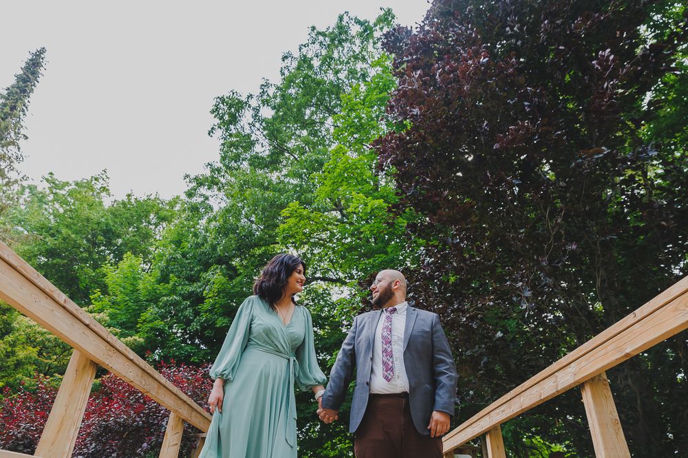 A couple holding hands while standing on wooden stairs surrounded by lush green trees.