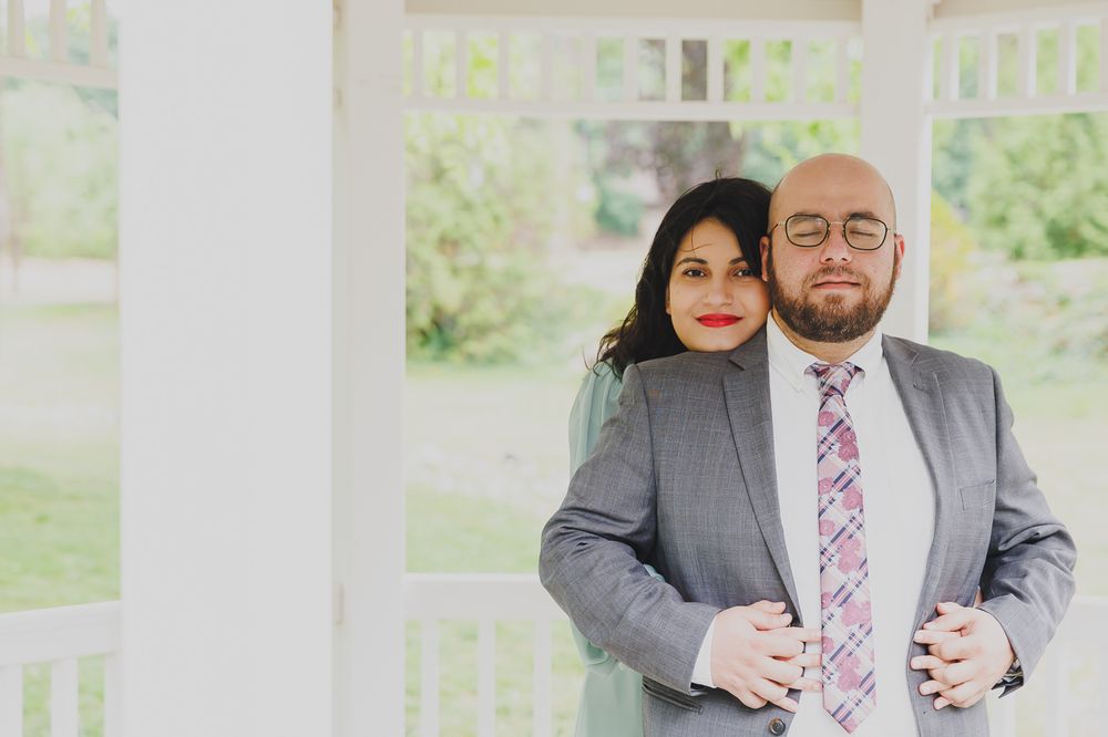 A couple standing apart on a wooden deck surrounded by lush forest scenery.