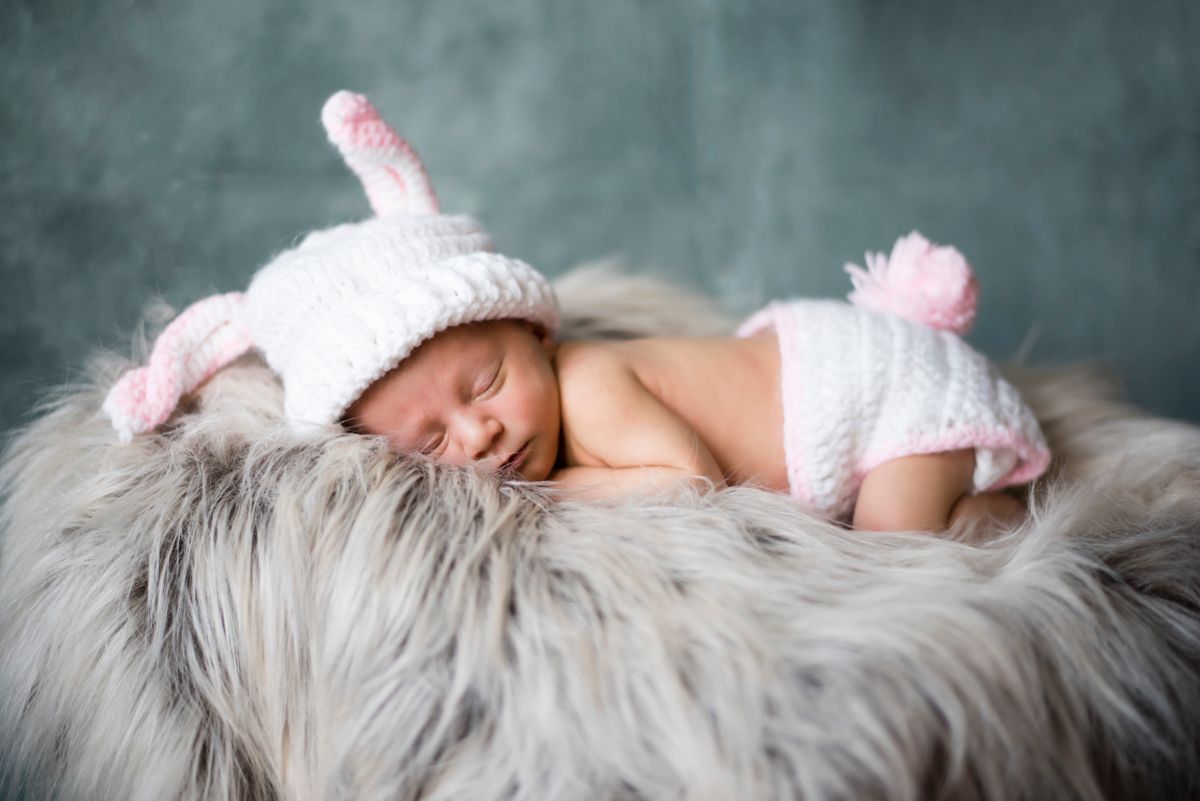 Newborn asleep in knit bunny outfit, on a faux fur bundle