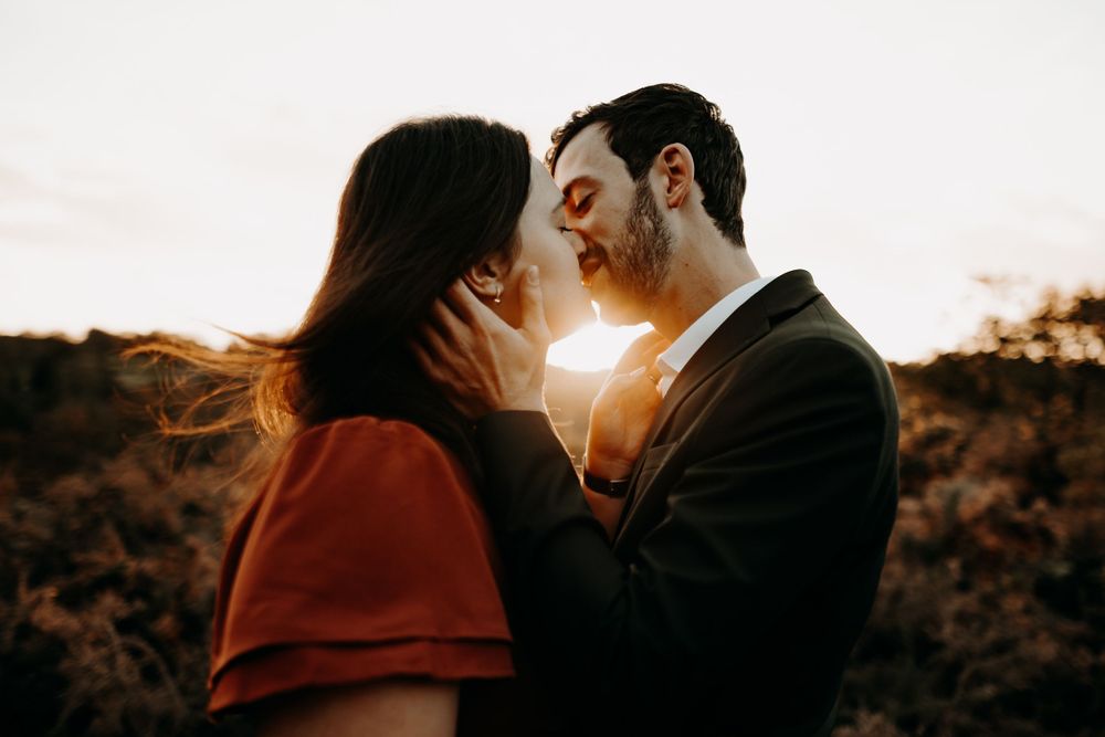 Silhouetted couple embracing during golden hour with sunlight peeking between them.