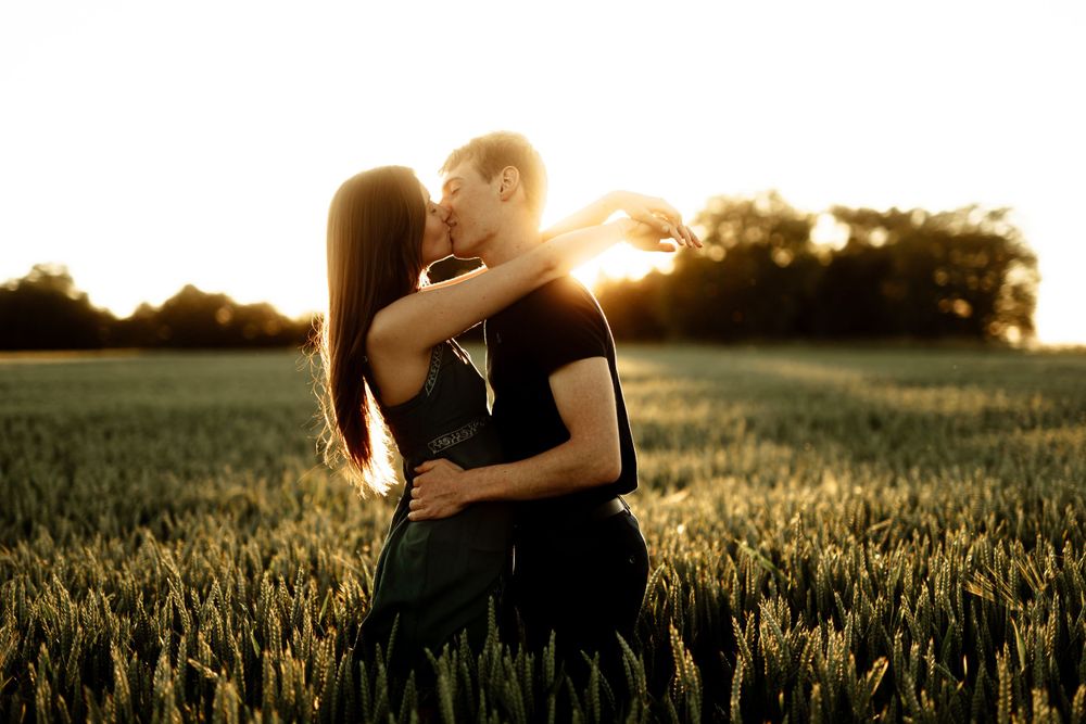 Romantic couple embracing in sunlit wheat field during golden hour.
