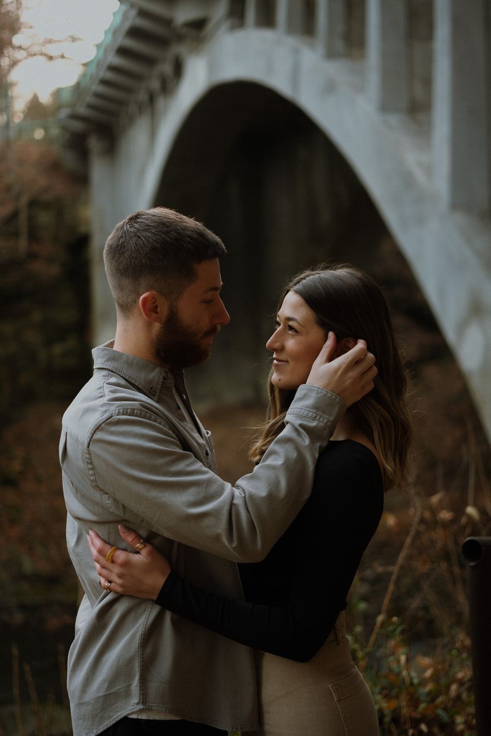 A tender moment shared between two people near a stone bridge in autumn.