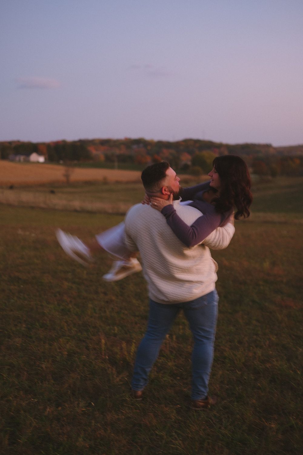 A couple dances and spins together in a field at sunset.
