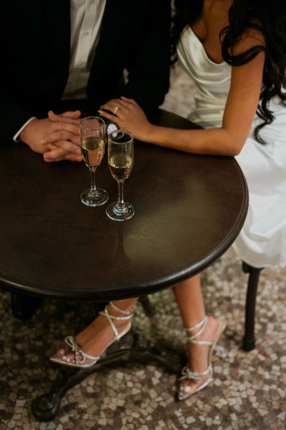 Detail shot of formal attire and wine glasses on dark table at evening event.