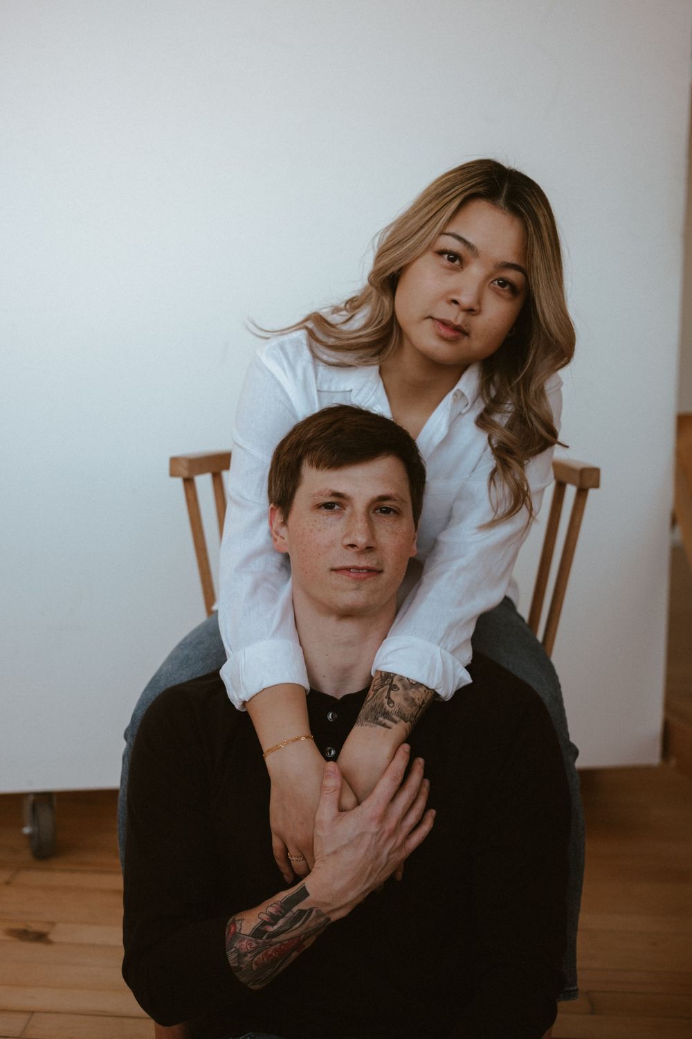 Indoor portrait session with minimalist white background and wooden chairs.