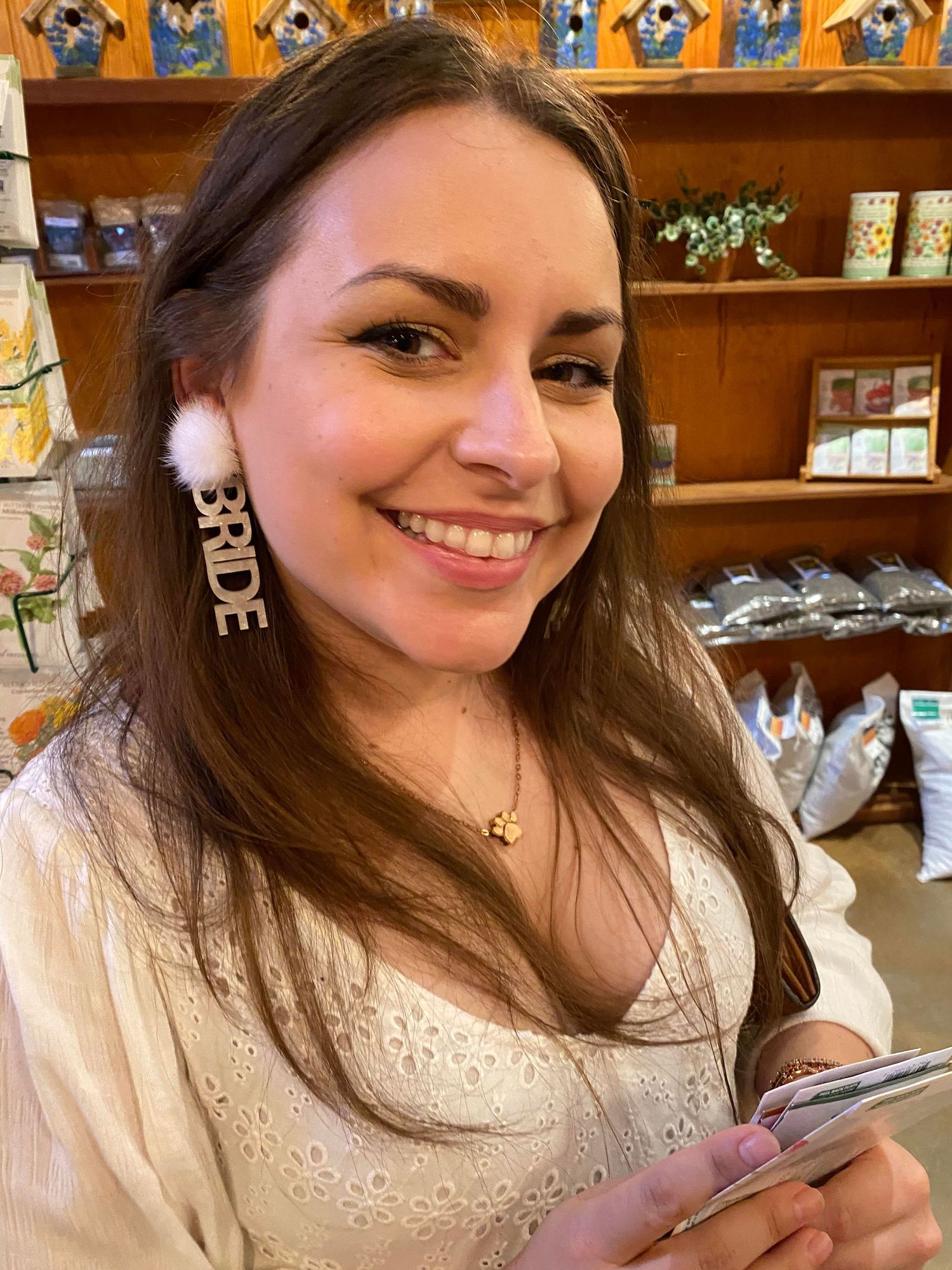 a brunette woman shows off large white dangle earrings that read "Bride"
