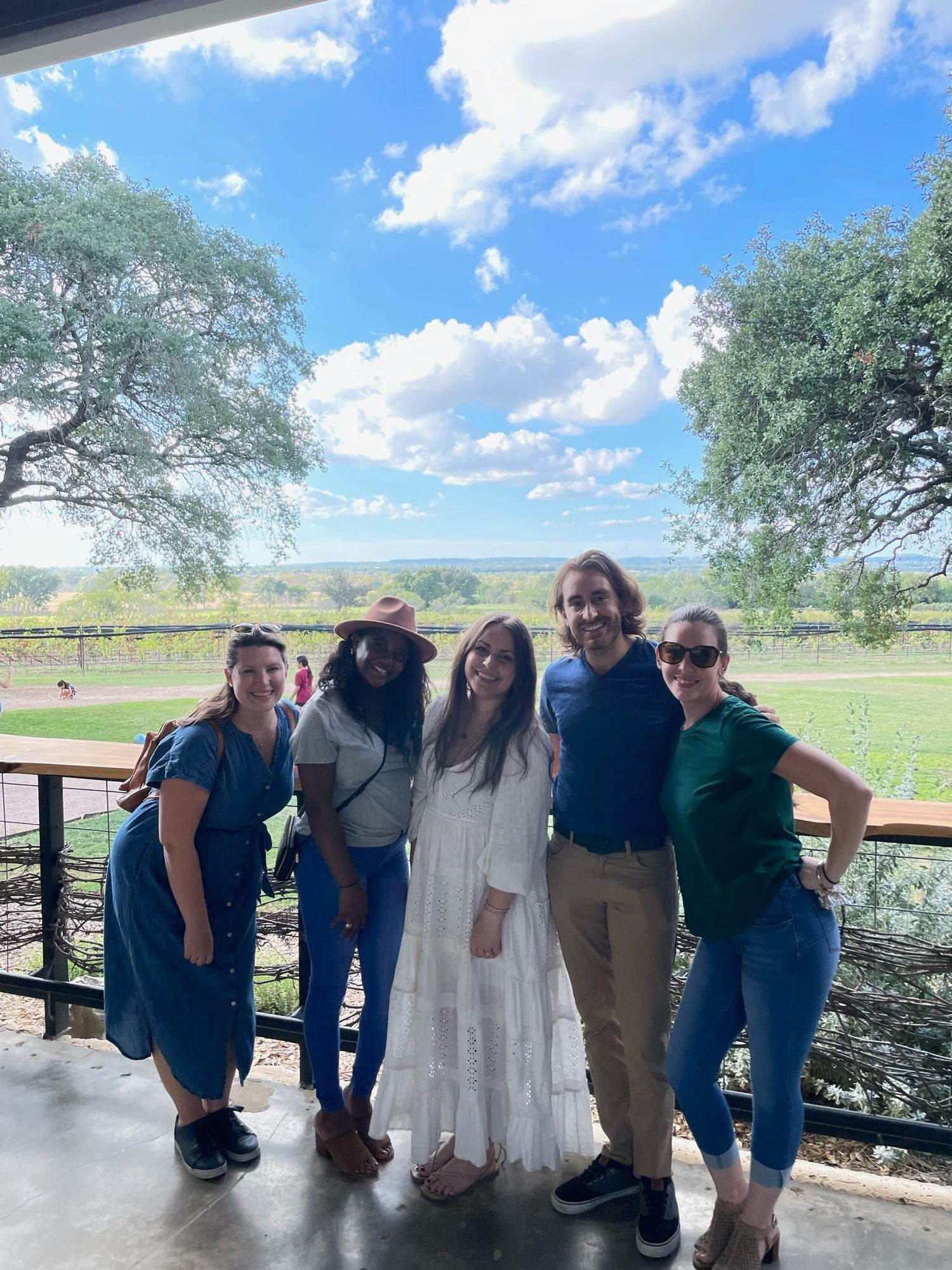 a group of four women and one man pose together in a line with a beautiful winery behind them