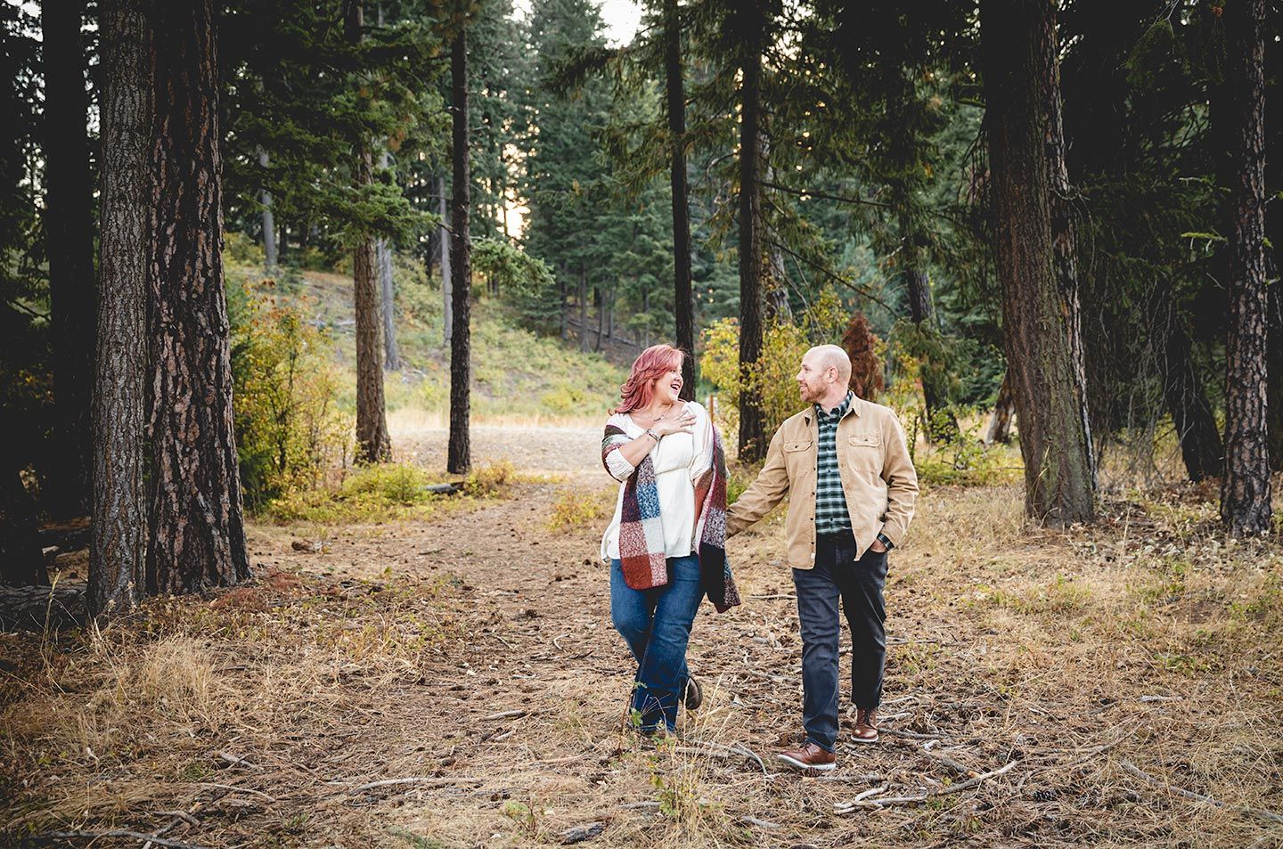 couple walking in between tall pine trees and holding hands