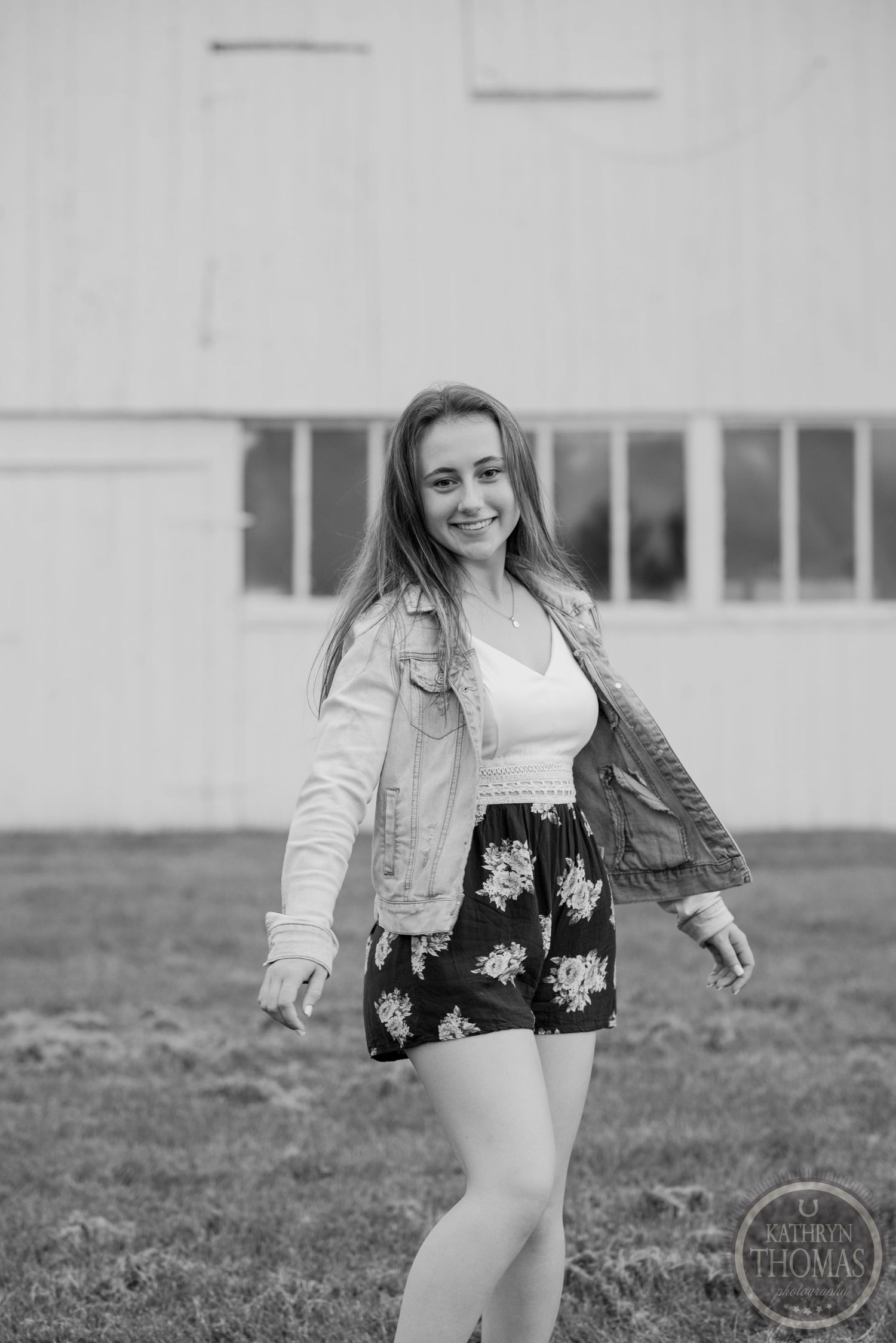 Black and white portrait of someone in denim jacket and floral shorts twirling outdoors.