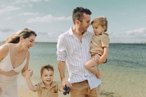 Joyful family on Cronulla beach with a smiling mother chasing her laughing son, while the father holds another kid