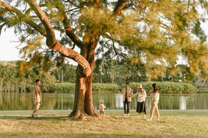 Extended family enjoying a walk by a lakeside under a majestic tree, in a tranquil outdoor scene of Centennial Park