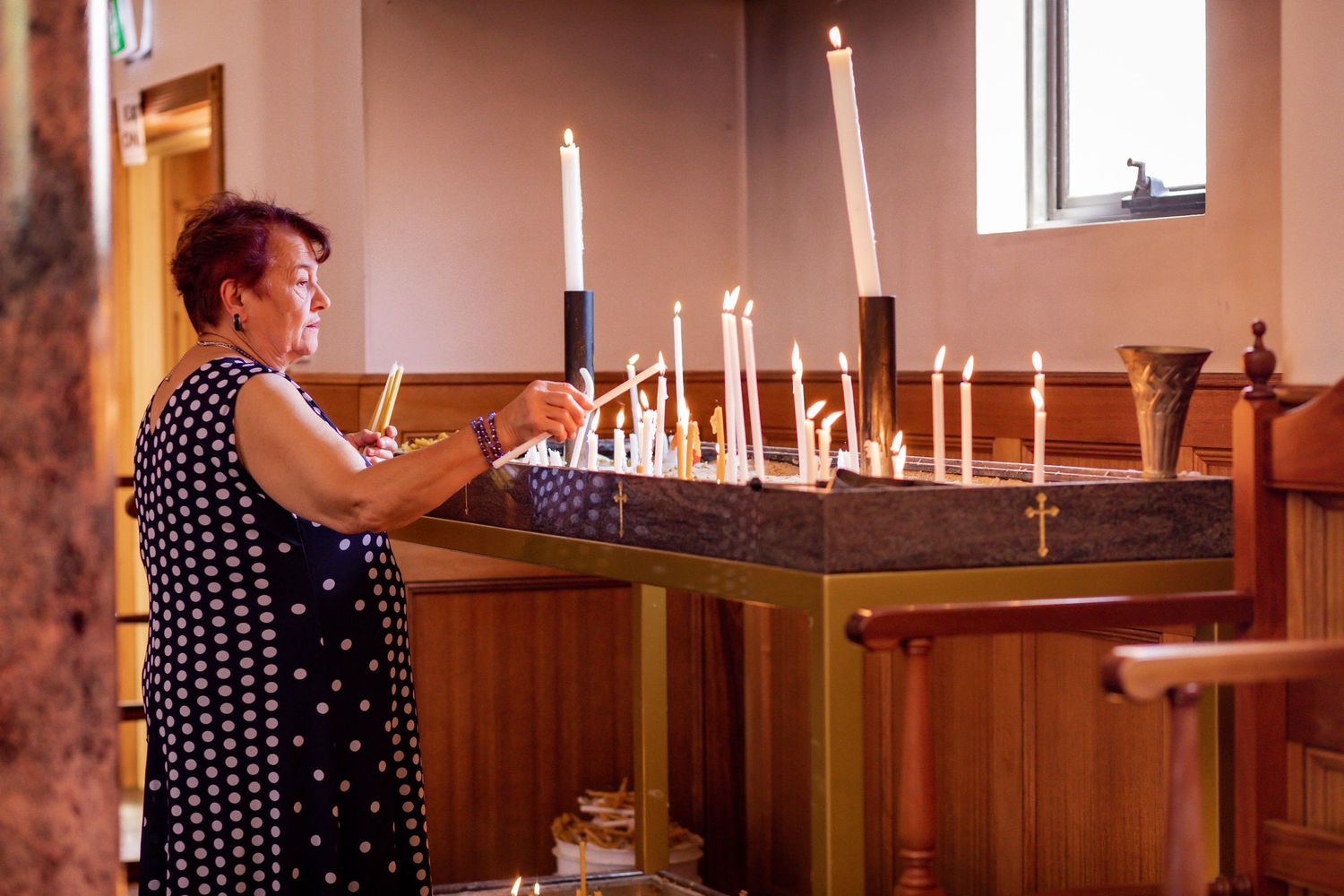 A person in polka dots lighting candles at a church altar.