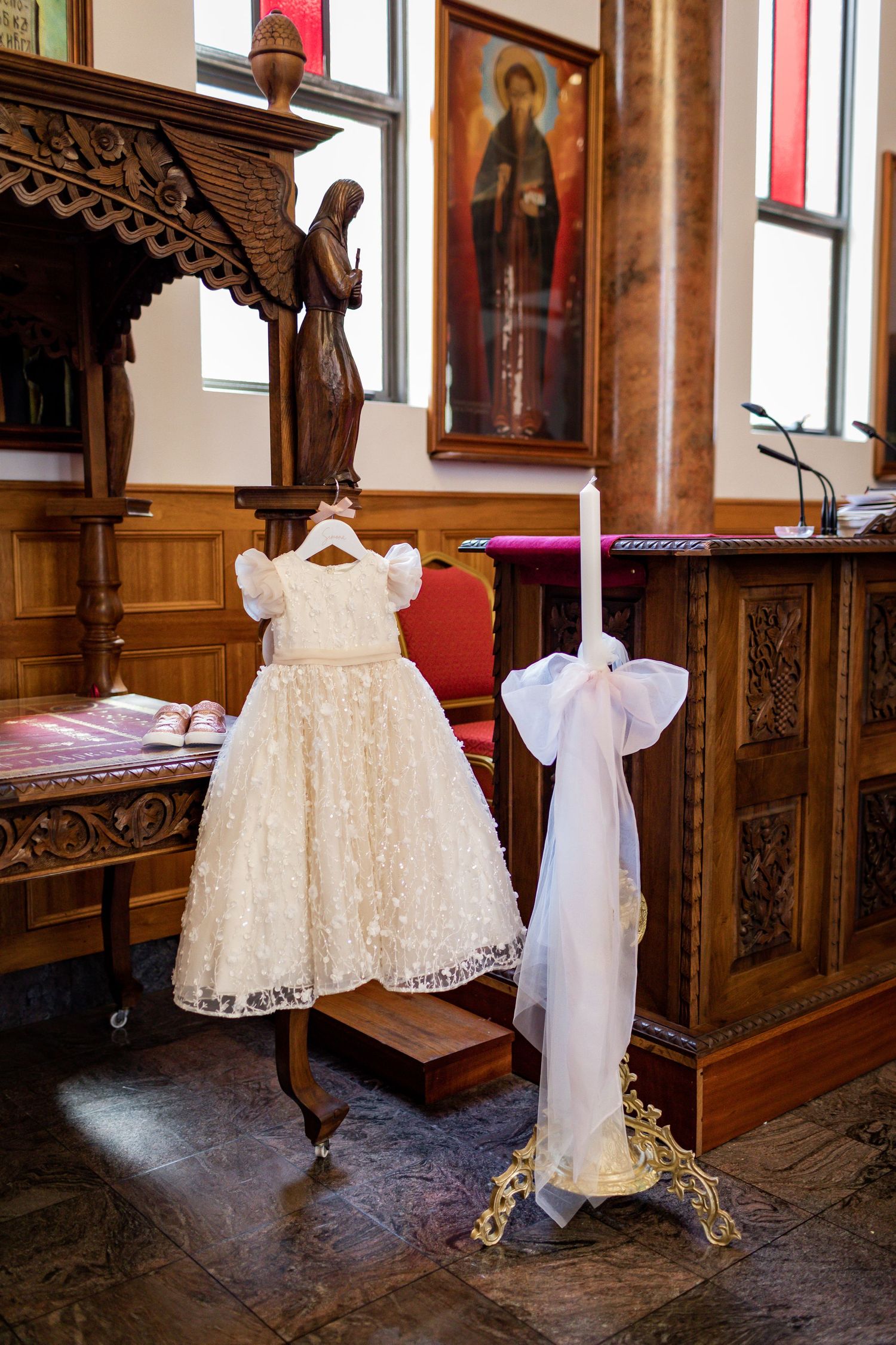 A white lace baptismal gown and christening candle displayed in a traditional church setting.
