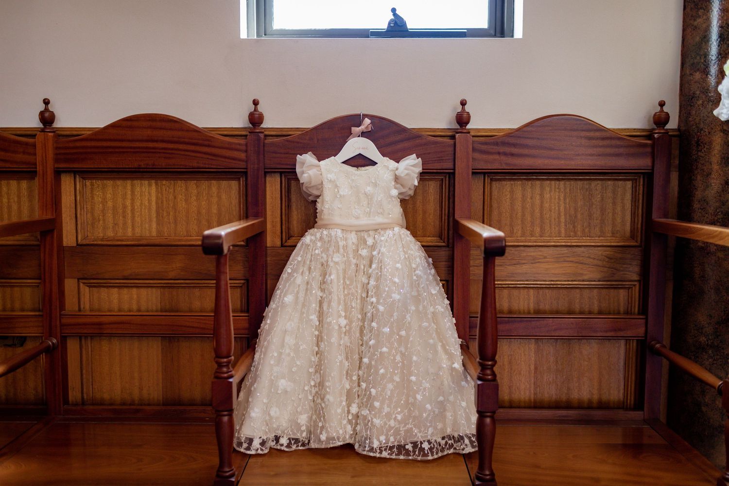 A white lace baptismal dress displayed on wooden church pew.