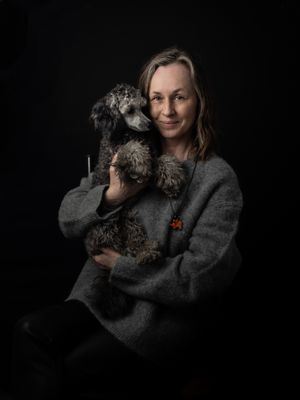 Dark moody portrait of someone in a grey sweater holding a scruffy mixed breed dog against black background.