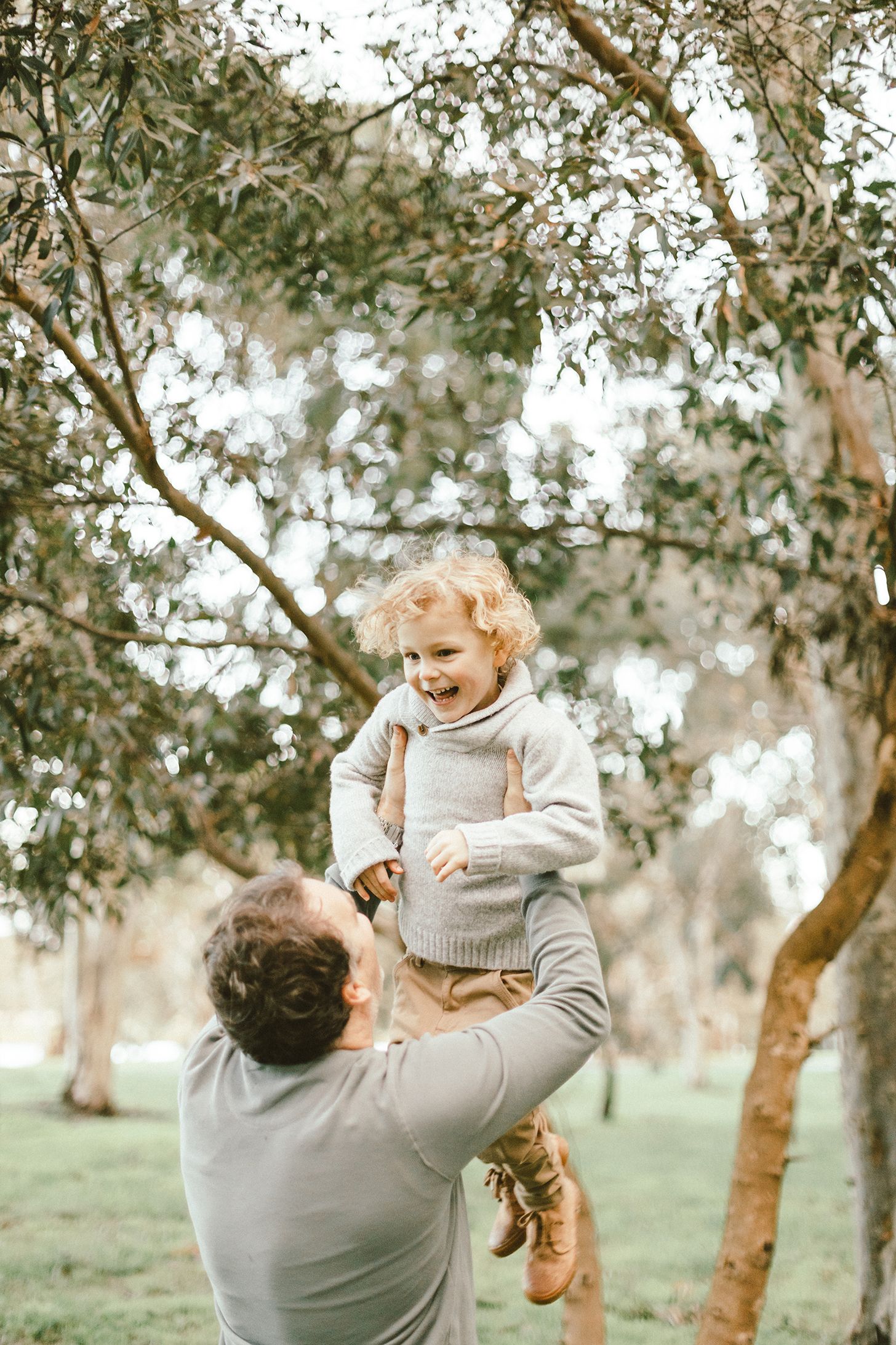 Parent playfully lifting a small child in the air among trees in a natural setting.