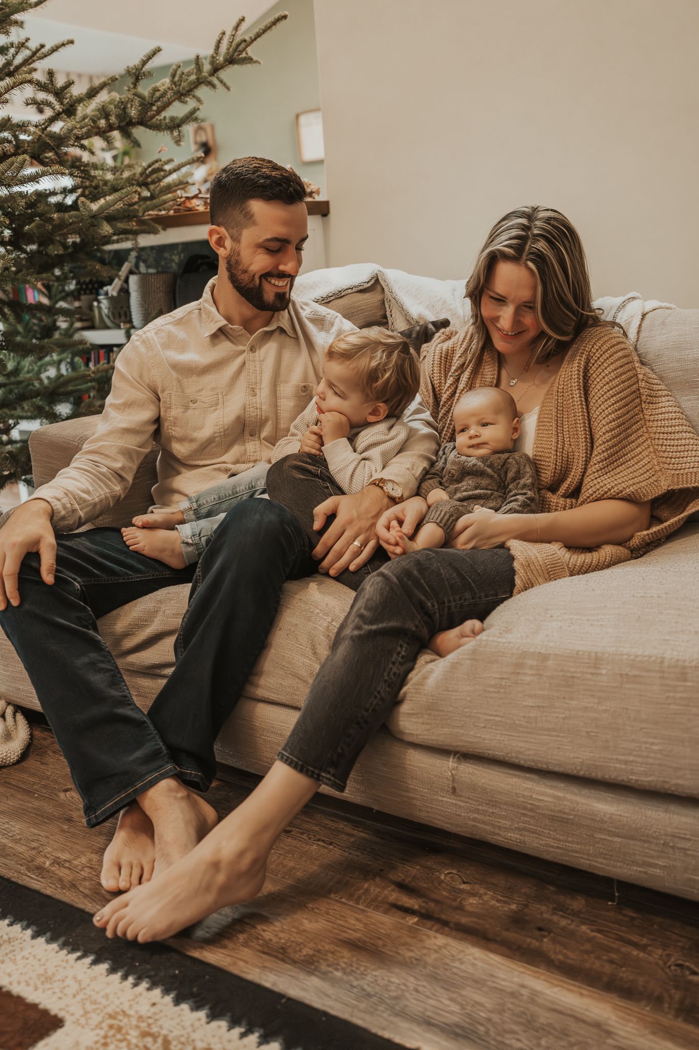 Family relaxing together on a cozy grey couch with a Christmas tree in the background.