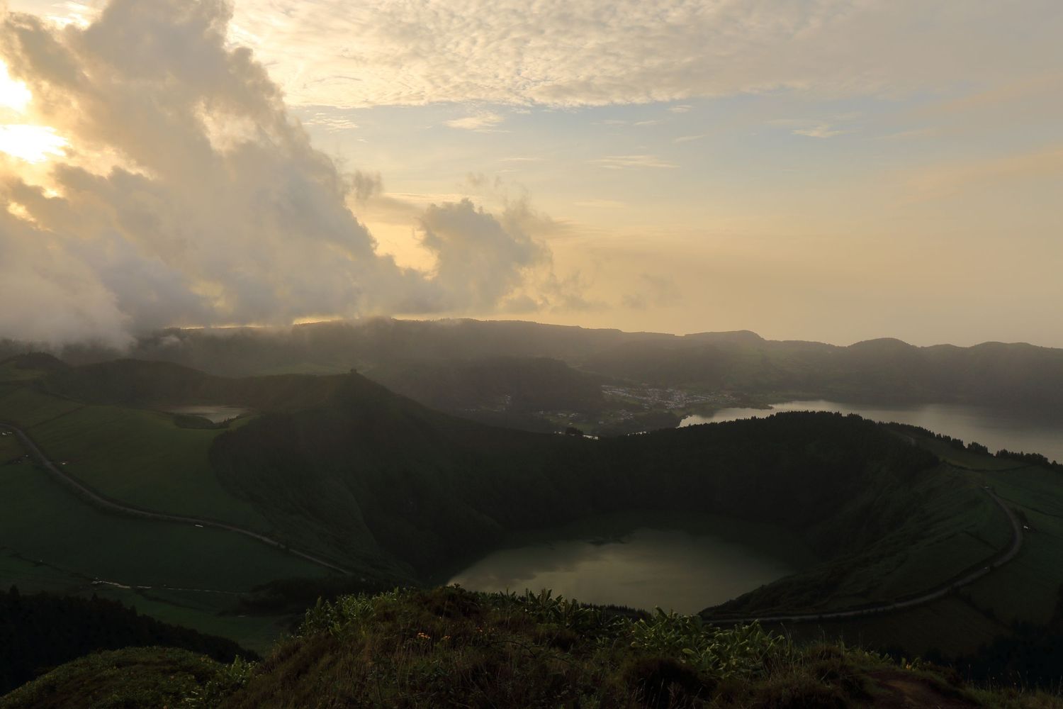 Two volcanic crater lakes surrounded by lush mountains at dusk with dramatic cloud formations.