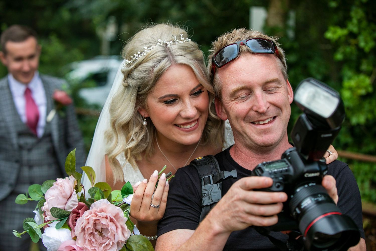 Wedding photographer shows couple images on camera display during outdoor photoshoot.