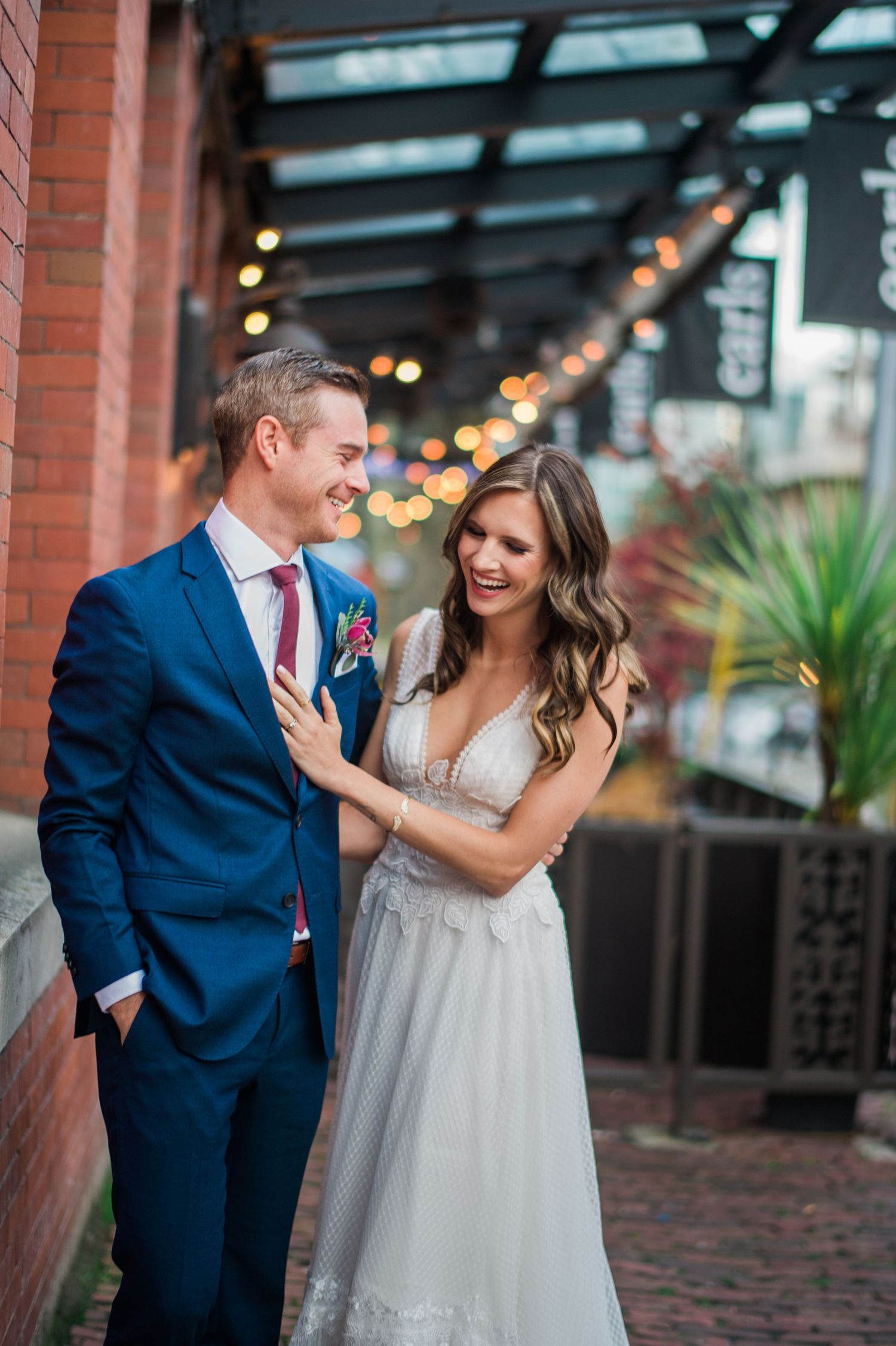 Wedding couple sharing an intimate moment against brick wall with string lights.
