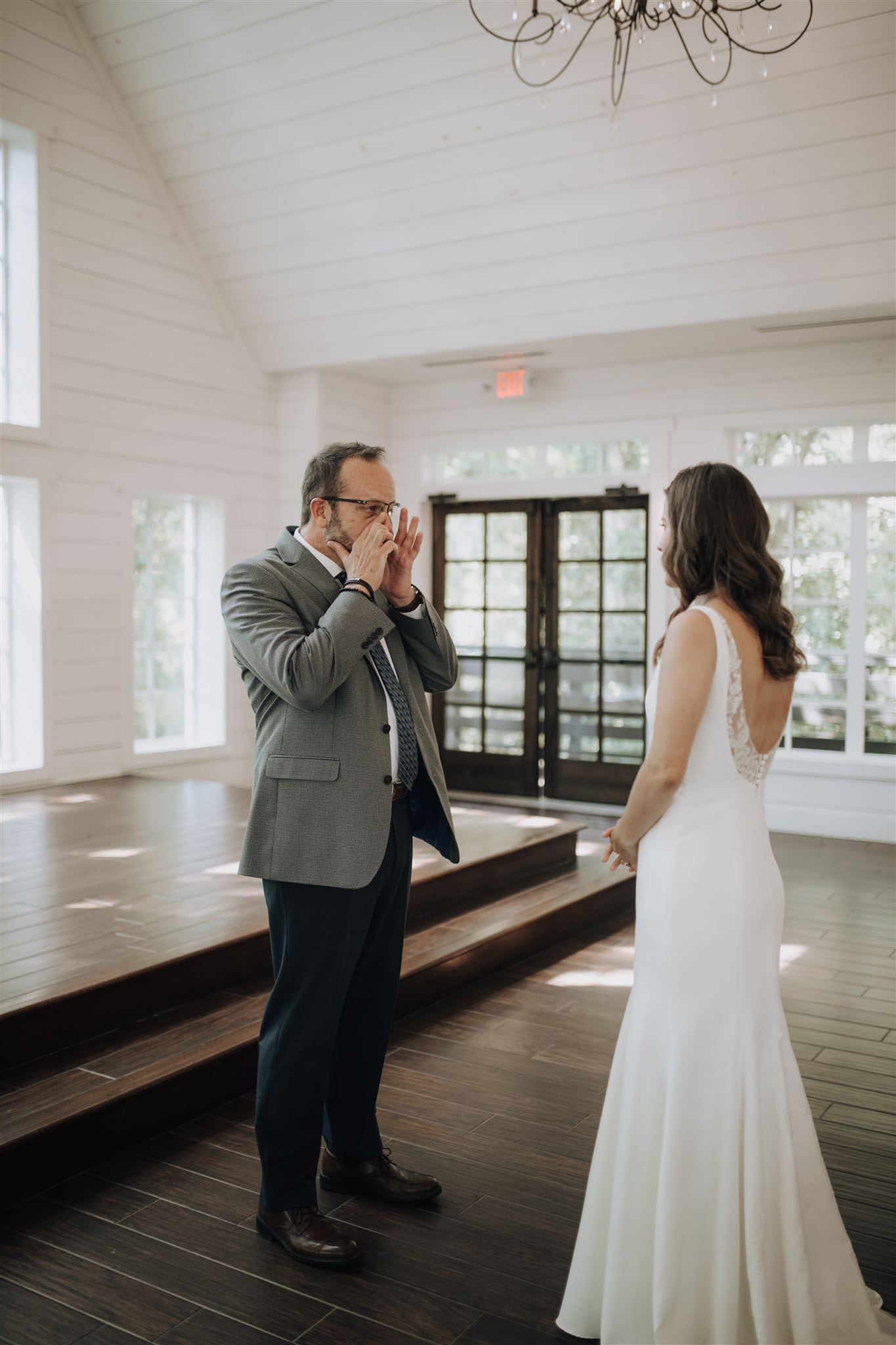 An emotional first look moment between a couple in a sunlit white chapel interior.