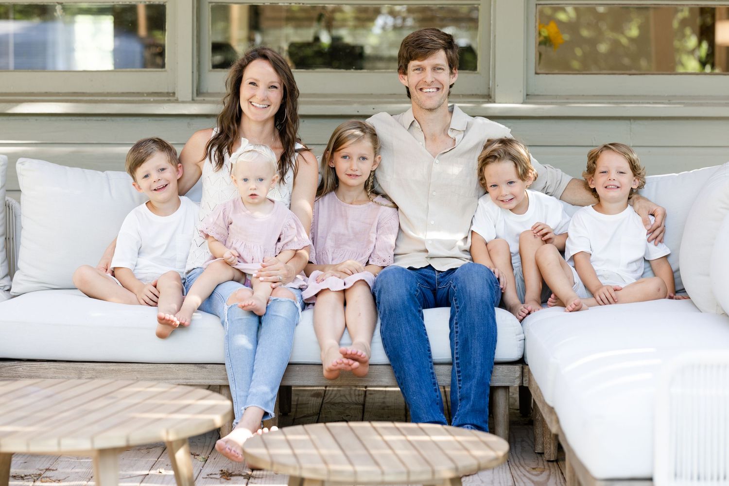 A family of seven are sitting on a white couch in their backyard happily photographed by Waco Photographer Blessie MJ