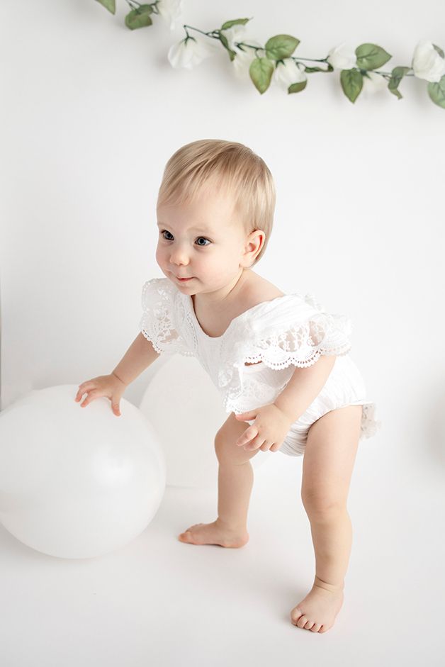 One year old girl standing and holding balance on white balloon.