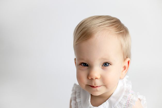 One year old girl smirking on a white backdrop.