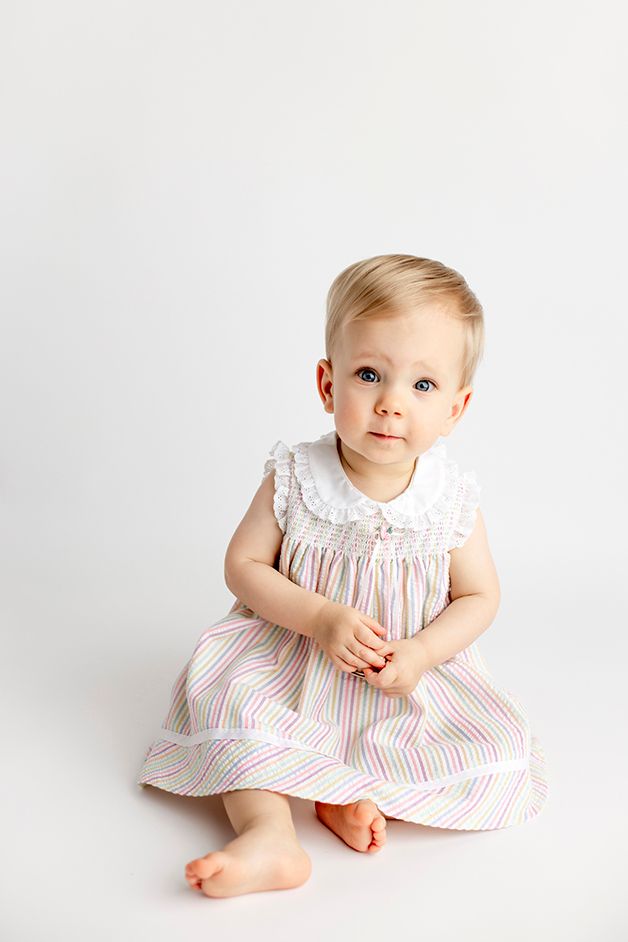 One year old girl in striped dress looking at the camera.