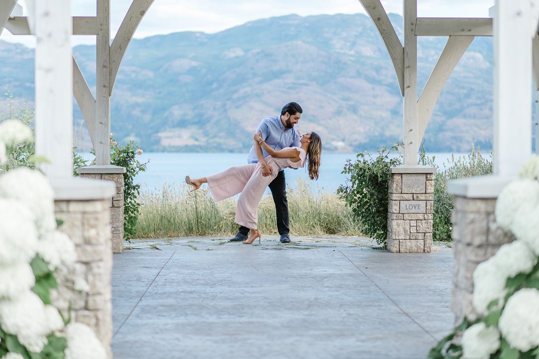 Couple embracing under a white pergola with mountain views and floral decorations.