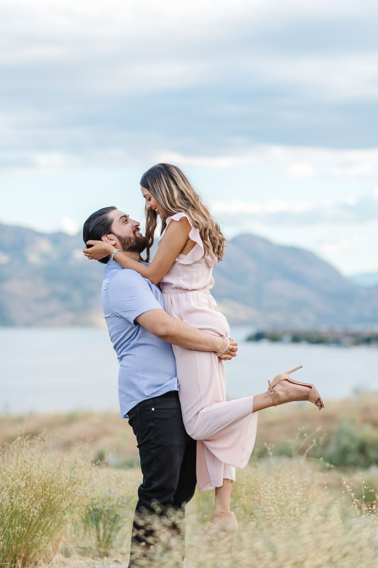 Playful couple dancing in a meadow with mountains and lake views.