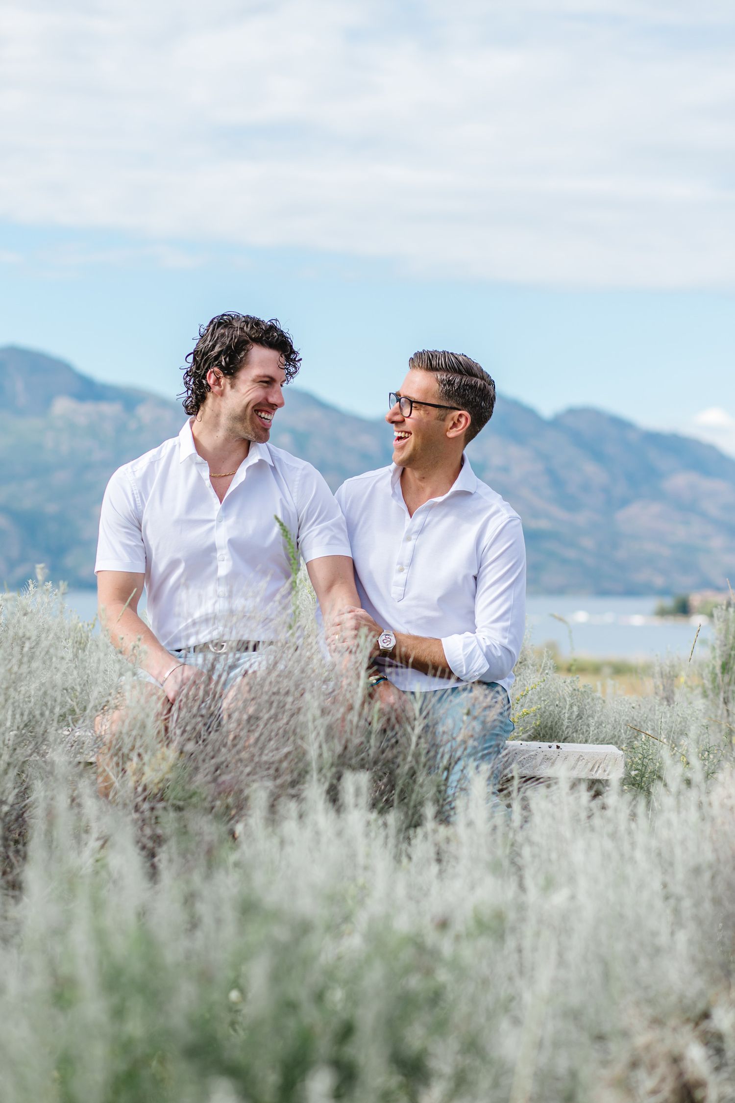 Two people sharing joyful laughter in a sage brush field with mountains behind.