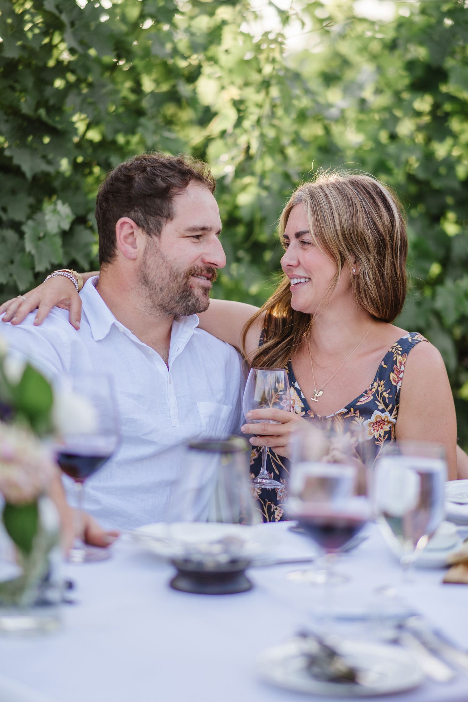 A couple shares an intimate moment at an outdoor dinner table with wine glasses.