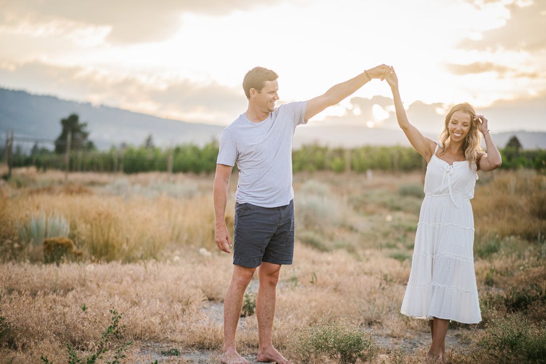 A couple dances and twirls together in a field during golden hour.
