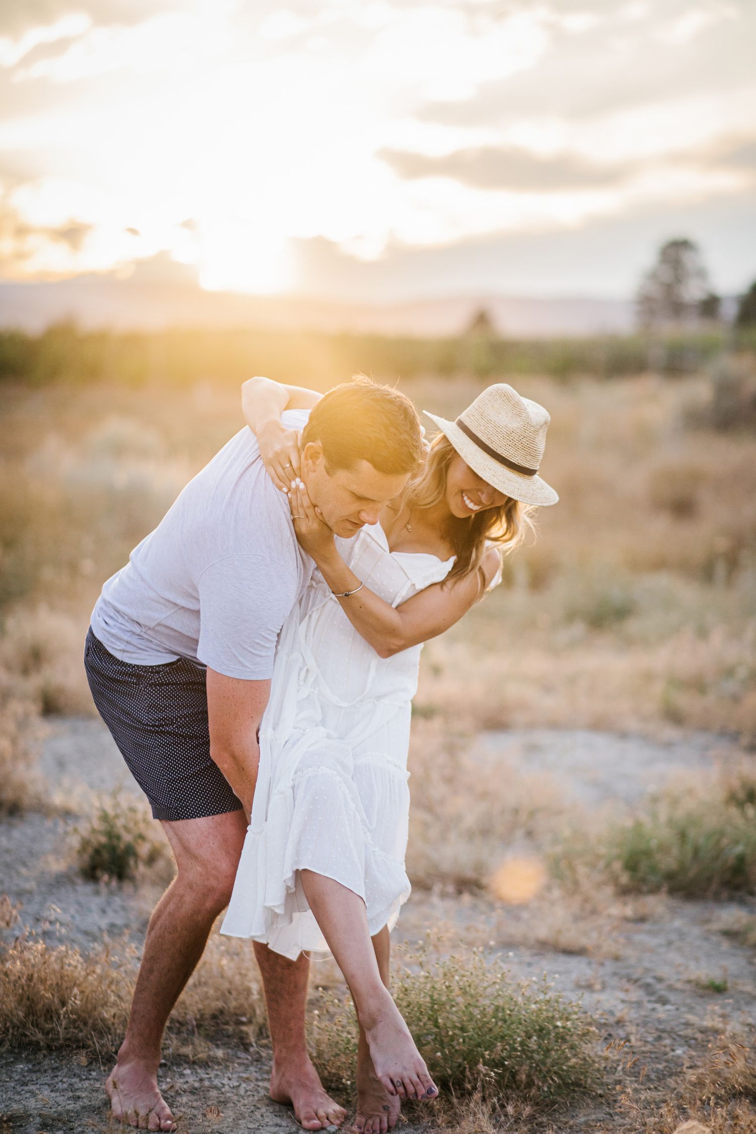 A couple laughs while dancing together in a desert field at sunset.