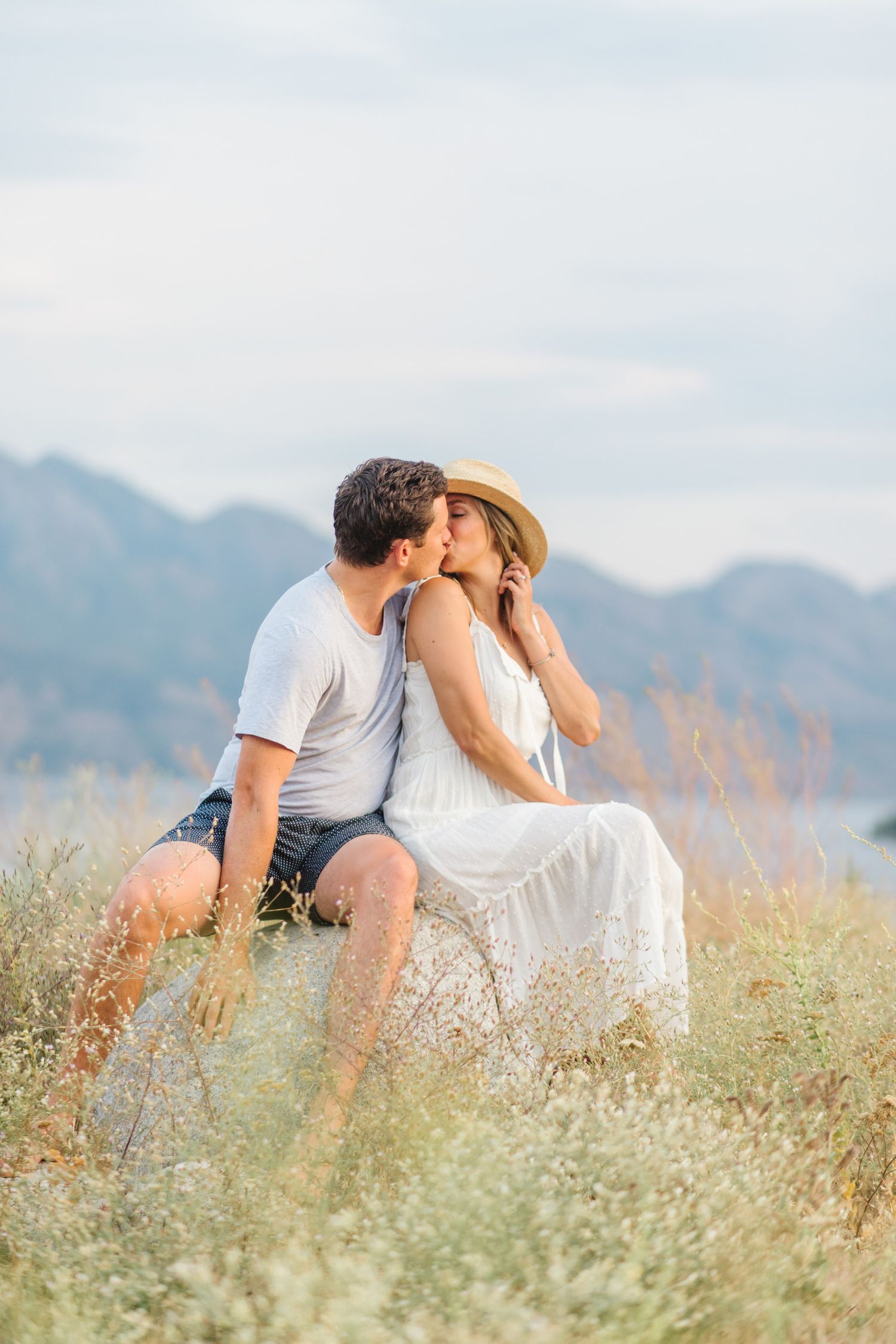 Romantic couple sitting in a wildflower field with mountains in the background.
