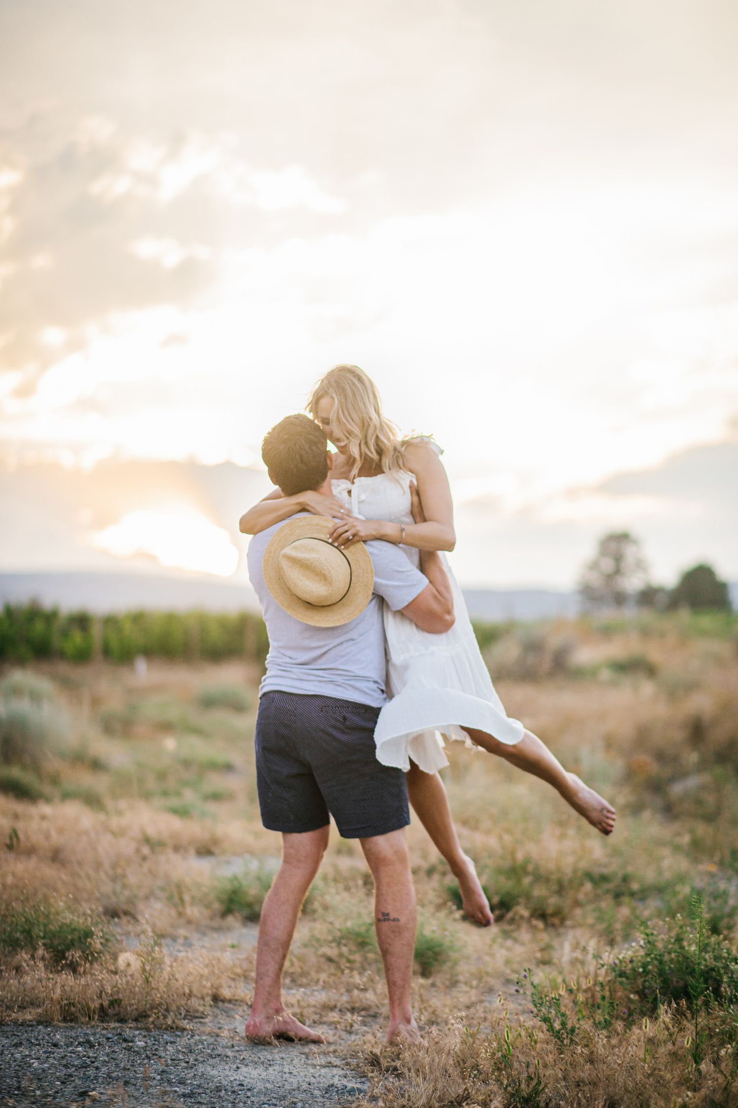 Playful couple dancing in field during sunset with mountains in distance.