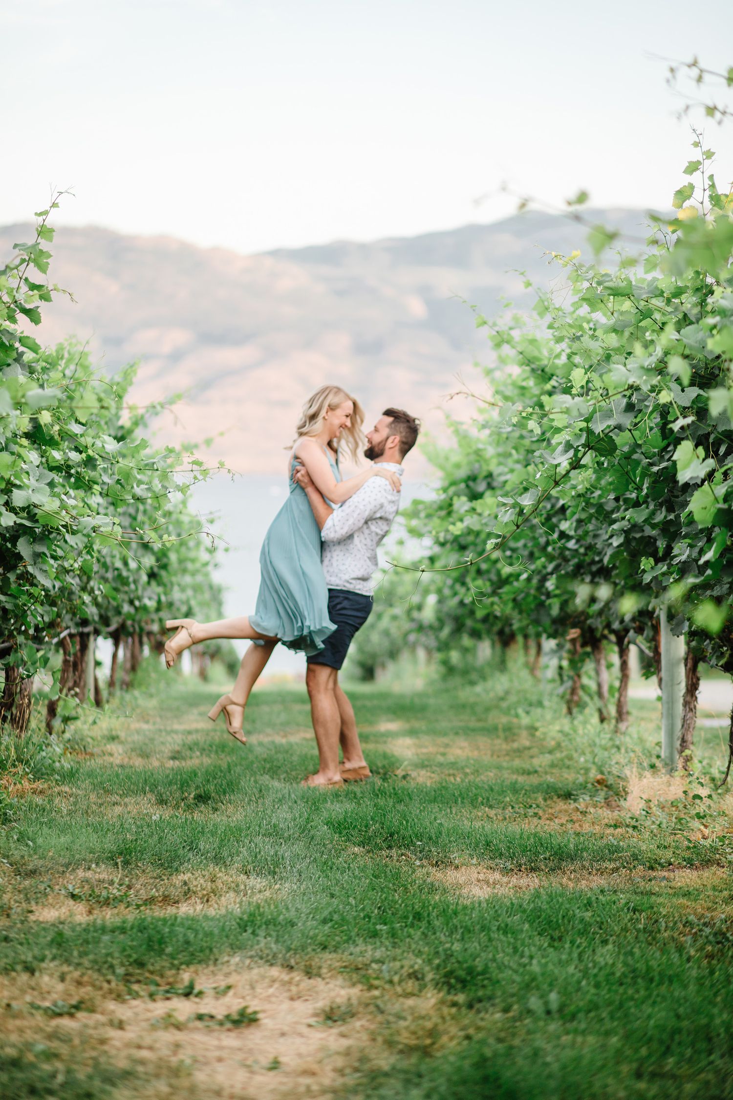 Couple sharing playful moment in vineyard with mountain backdrop.