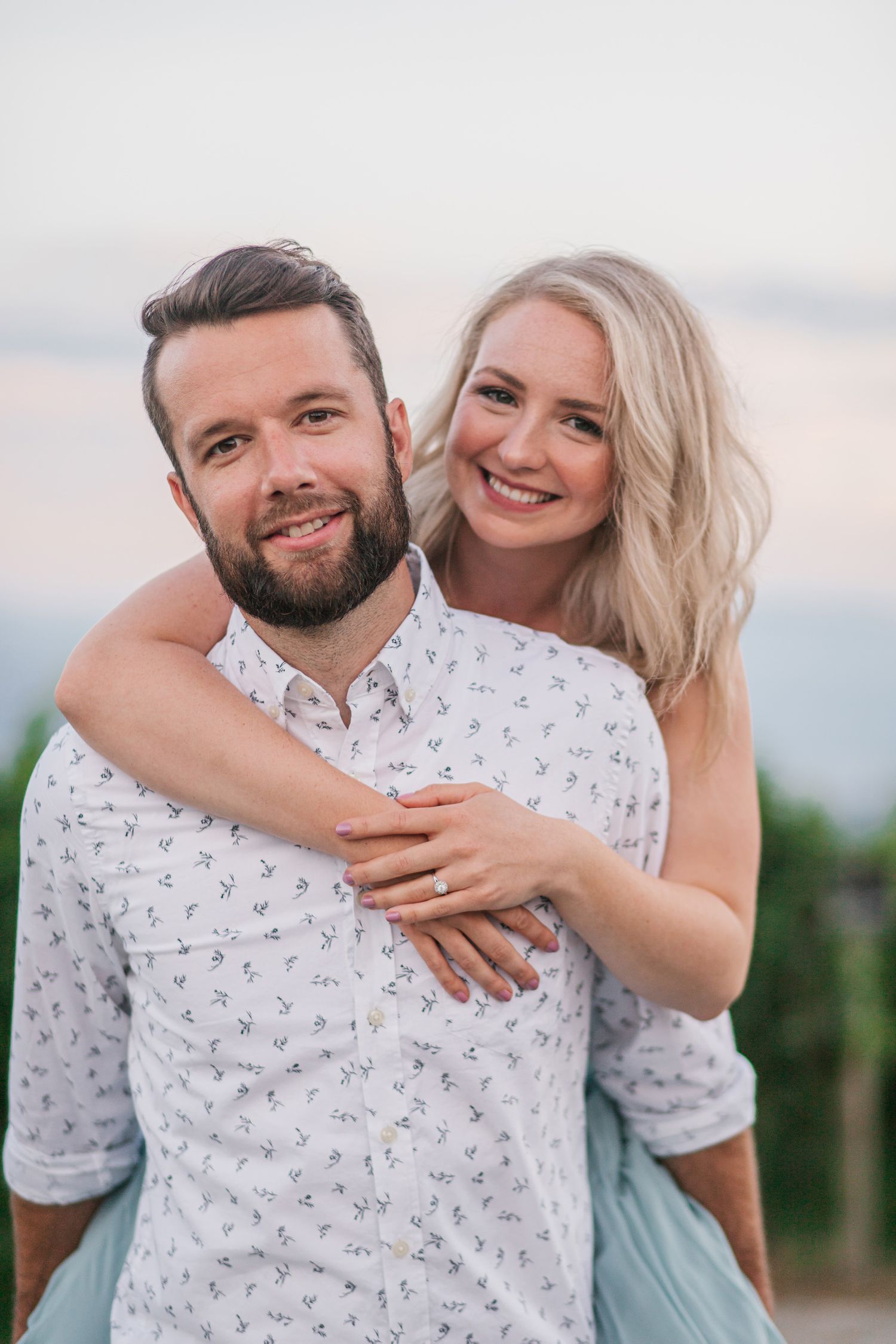 A couple embraces in casual attire against a natural outdoor setting during a photo session.