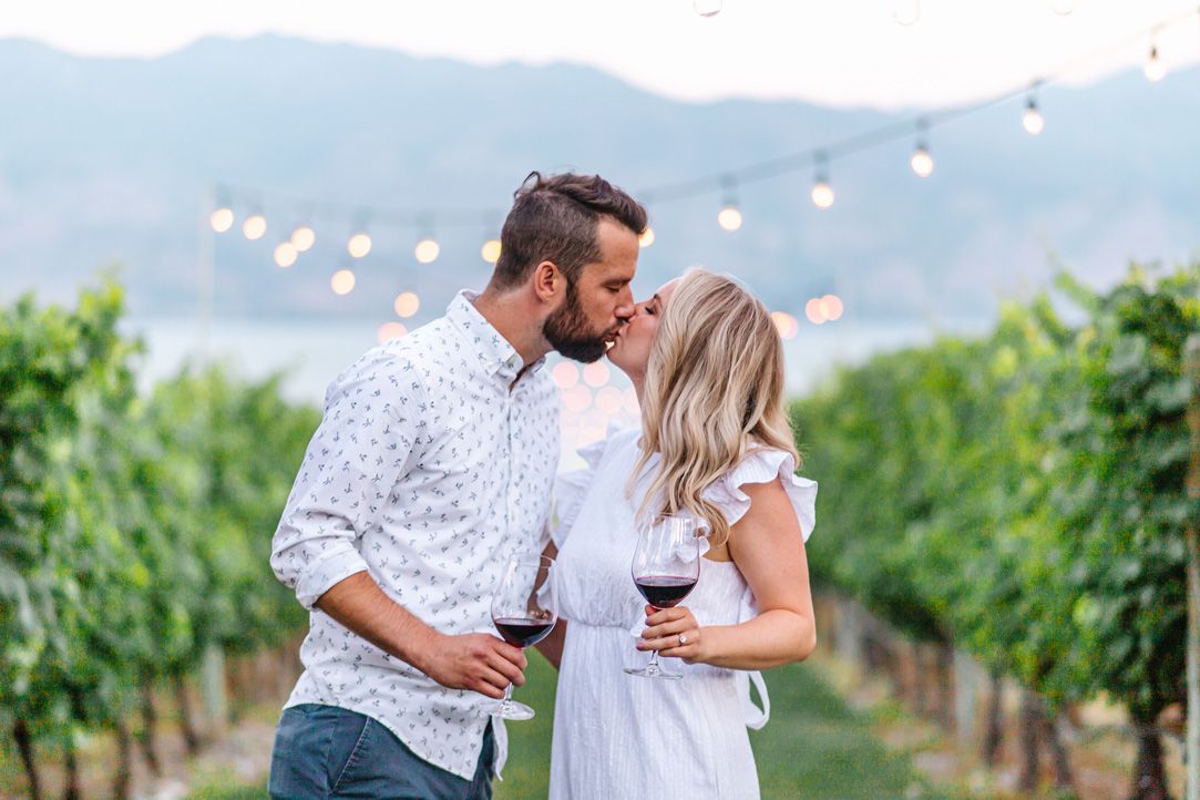 A couple shares an intimate moment among vineyard rows during sunset.