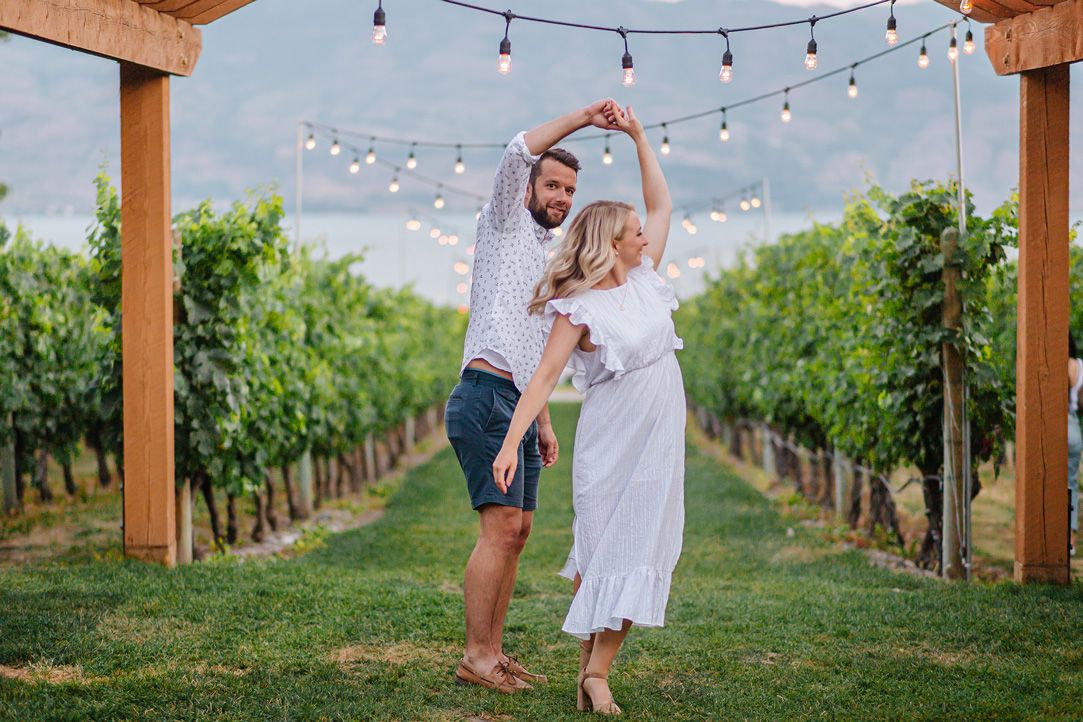 String lights hang over rows of grapevines in a romantic vineyard setting at dusk.