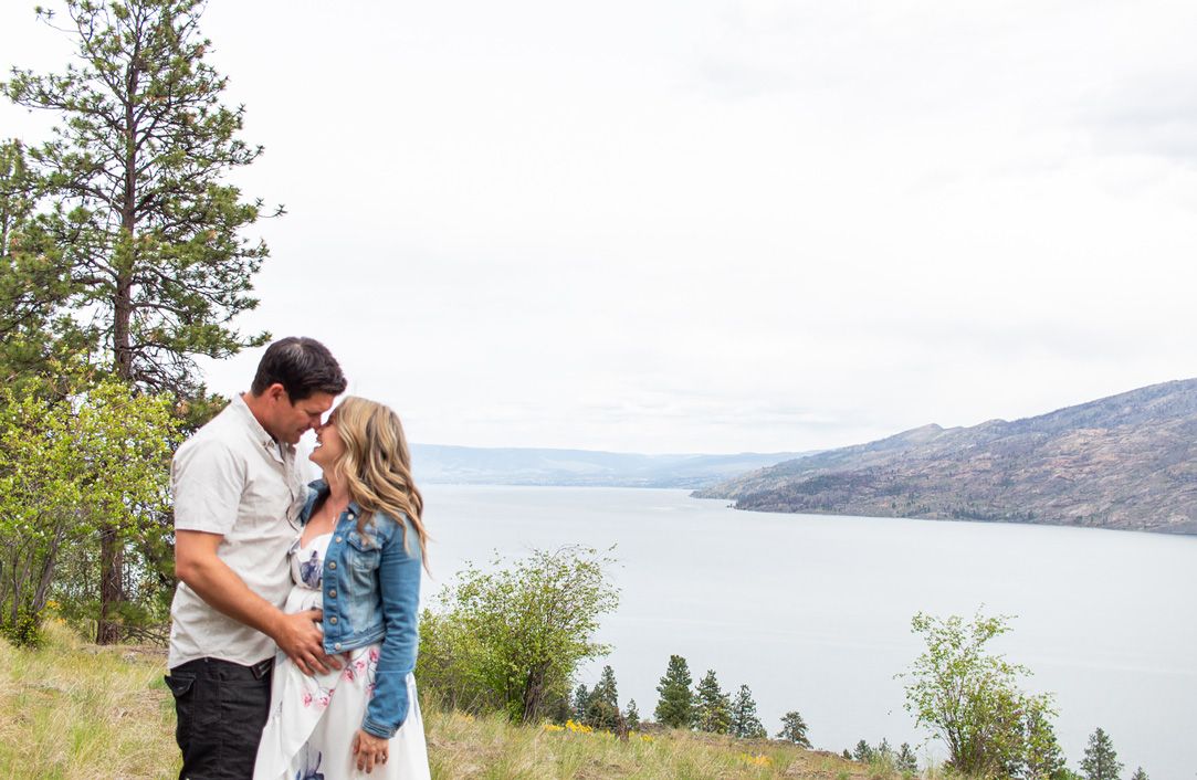 A scenic panoramic view of a lake and mountains with two people in silhouette.