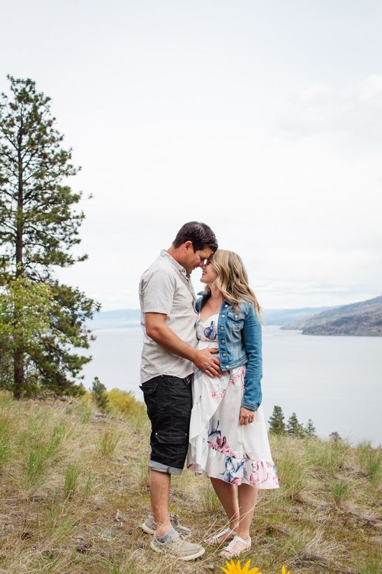 A couple shares a romantic moment on a hillside overlooking a scenic lake view.