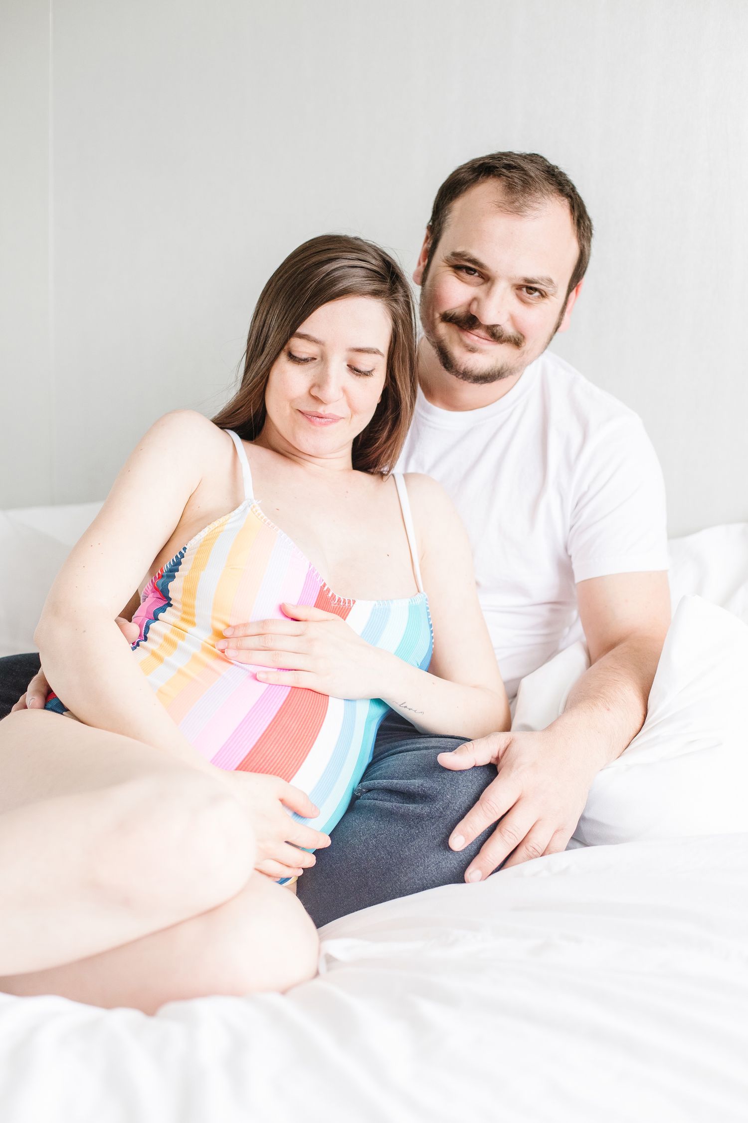Couple sharing intimate moment while lounging on white bedding during lifestyle shoot.