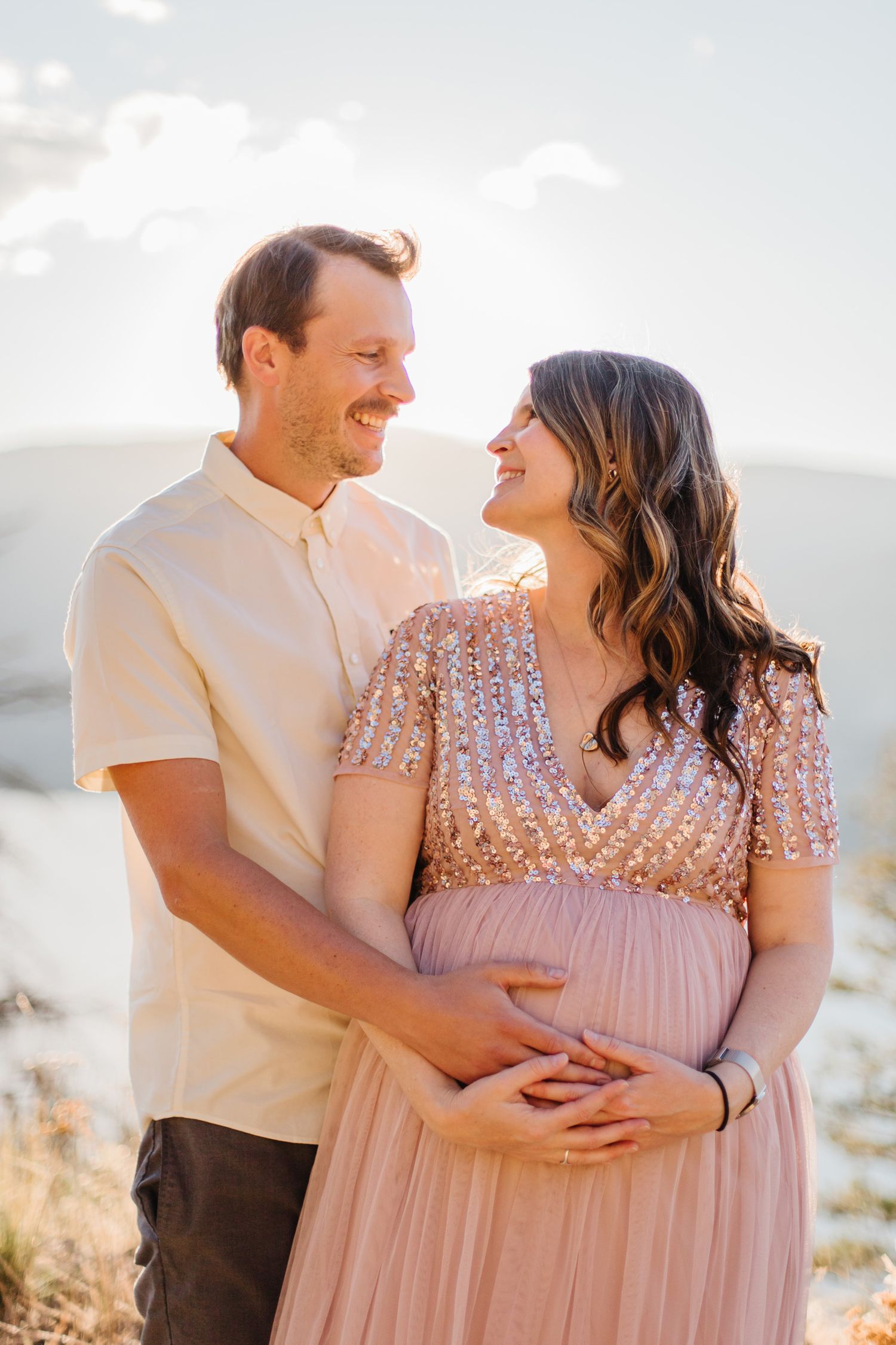 A couple in formal attire shares tender moments during a sunset photoshoot.