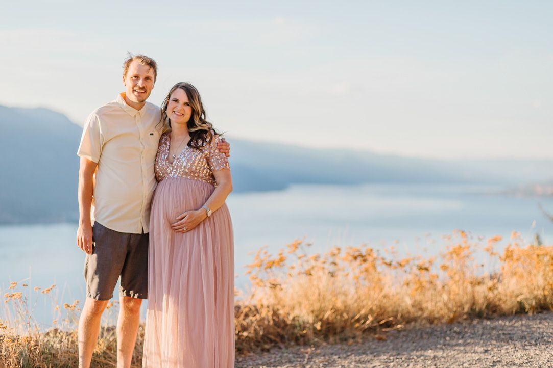 A couple poses together in a golden field during sunset for maternity photos.