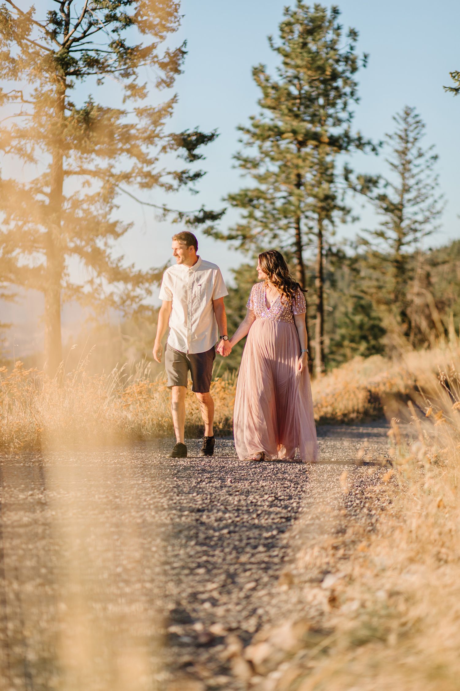 Couple sits together on rocky ground at sunset with pine trees in background creating romantic autumn ambiance.