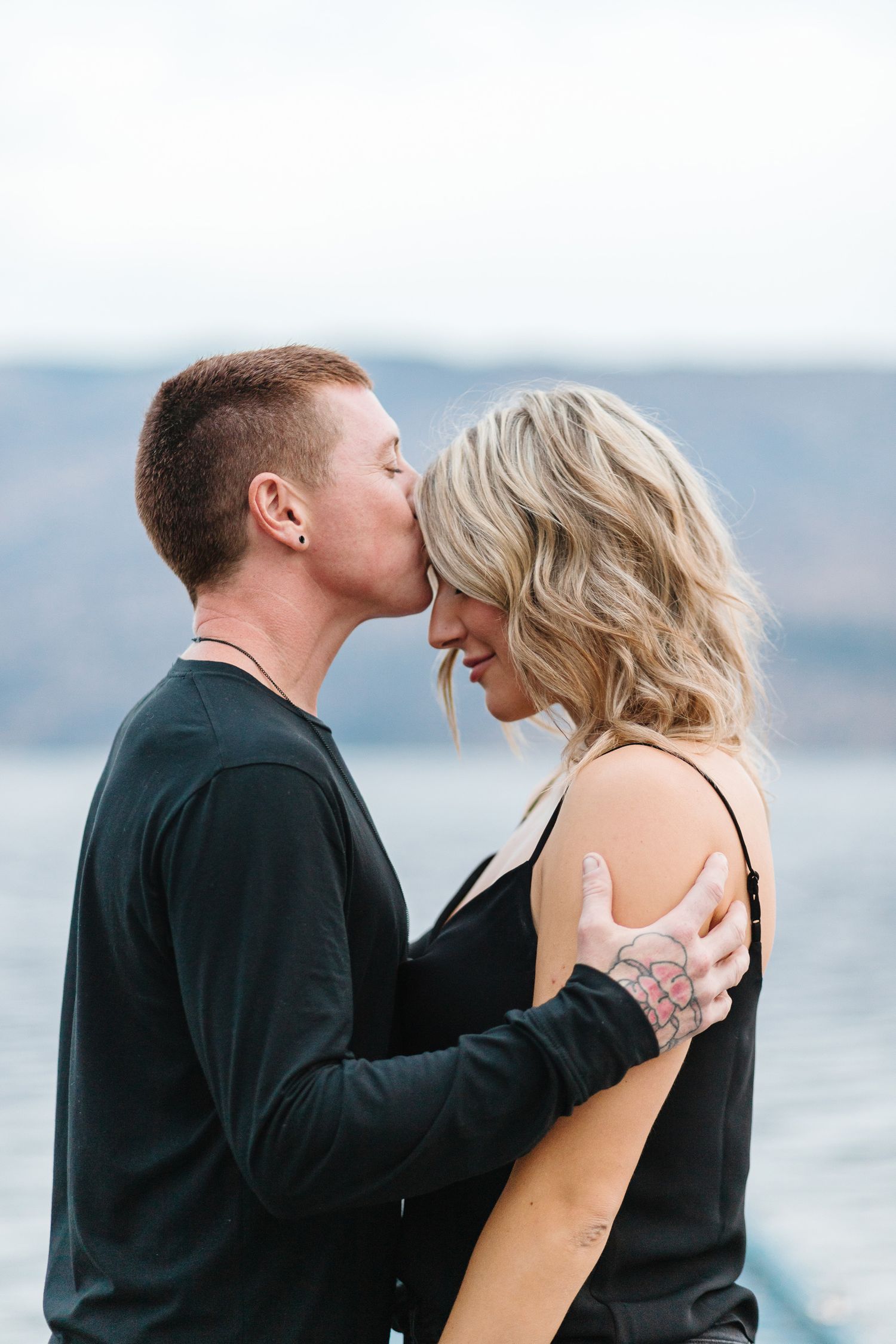 Intimate couple shares tender moments on lakeside dock during photo session.